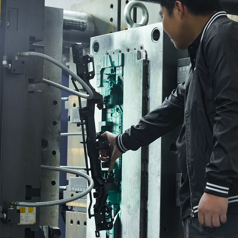 Los empleados de FirstMold'retiran manualmente las piezas de plástico de la máquina de moldeo por inyección.